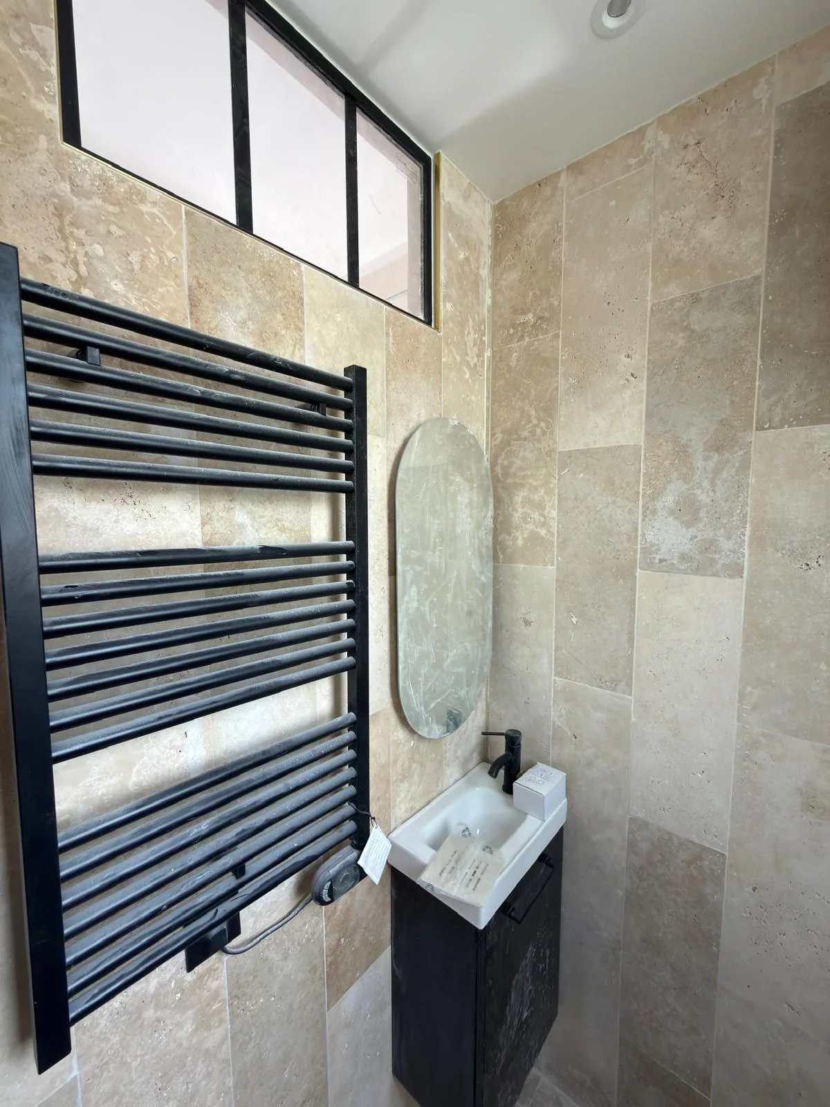 Verrière d'atelier, miroir ovale et sèche-serviettes noir sur mur en travertin